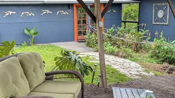 An outdoor seating area with a wicker sofa and a table, surrounded by gravel and plants.