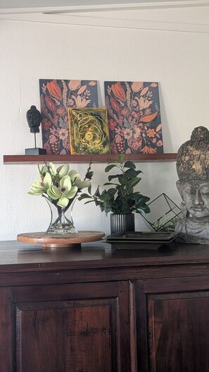 A wooden cabinet with decorative items including a Buddha head sculpture, a vase with flowers, and two framed artworks.