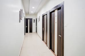 A corridor with doors numbered 100 to 107, white walls, and framed pictures on the left. - Townhouse Faizabad Road Opp BBD (Lucknow)