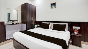 A hotel room with a large bed, a wardrobe, a bedside table with a lamp, and a nightstand with a vase of flowers. - Townhouse Faizabad Road Opp BBD (Lucknow)
