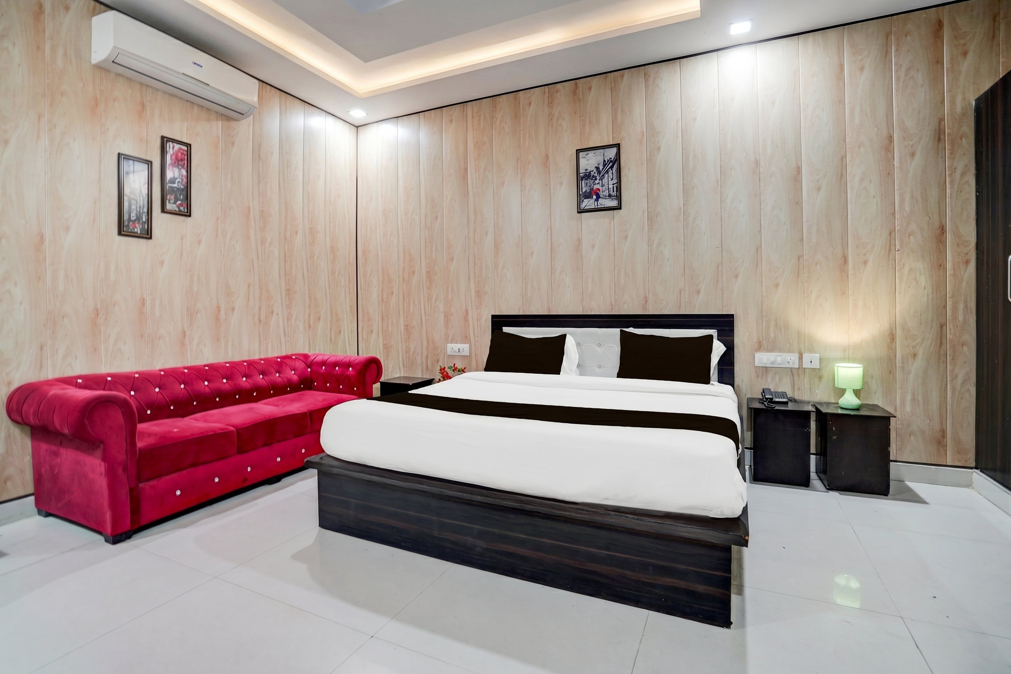 A modern bedroom with a large bed, a red sofa, and wooden panel walls.