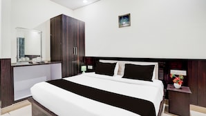 A hotel room with a large bed, a wardrobe, a bedside table with a lamp, and a small nightstand with a vase of flowers. - Townhouse Faizabad Road Opp BBD (Lucknow)