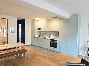 Eine moderne Küche mit hellen Schränken, einer eingebauten Mikrowelle und einem Backofen. Im Vordergrund steht ein Esstisch mit einer Bank.