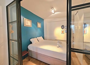 Ein Schlafzimmer mit einem Bett, einem kleinen Tisch und einer Wand mit gerahmten Bildern.