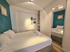 Ein Hotelzimmer mit einem großen Bett, einem Nachttisch, einem Spiegel und einer eingebauten Bücherreolen.
