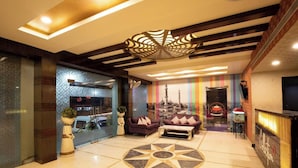 A hotel lobby with a modern design, featuring a central seating area with a patterned floor, a decorative ceiling, and a view of a mosque through the glass wall. - Townhouse Oak Varanasi Ganga Ghat (Varanasi)