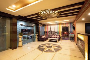 Um saguão de hotel com design moderno, apresentando uma área de estar central com piso estampado, teto decorativo e vista para uma mesquita através da parede de vidro.