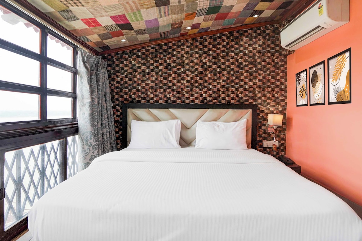 Quarto de hotel com uma cama grande, parede com padrão de tijolos e uma janela com cortinas.