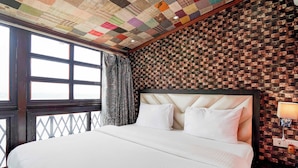 A hotel room with a large bed, a patterned ceiling, a brick wall, and a window with curtains. - Townhouse Oak Varanasi Ganga Ghat (Varanasi)