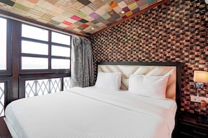 Quarto de hotel com cama grande, teto estampado, parede de tijolos e janela com cortinas.