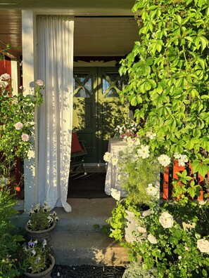 A garden entrance with a covered porch, potted plants, and a table with a white tablecloth.