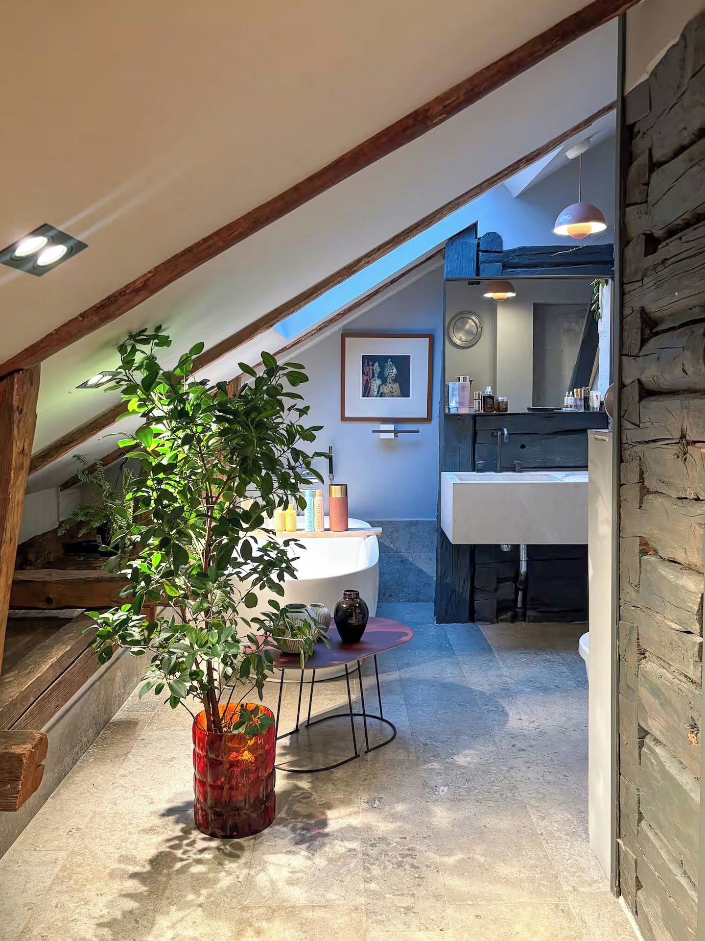 A cozy attic space with a wooden ceiling, a dining table with chairs, a potted plant, and a kitchen area with a sink and countertop.