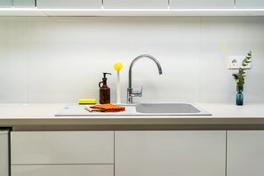 Eine moderne Küche mit Spüle aus Edelstahl, einer Seifenspender, einem gelben Schwamm und einem orangefarbenen Stoffhandtuch.