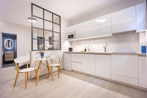 Eine moderne Küche mit weißen Schränken, einer eingebauten Mikrowelle und einem Essbereich mit Tisch und Stühlen.
