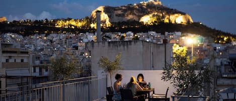 Una terraza en la azotea con vistas a un paisaje urbano en una colina, incluyendo una colina destacada con luces.