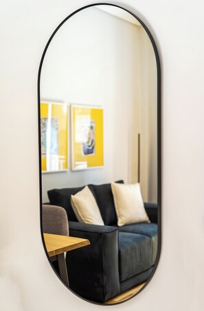 A mirror reflecting a room with a dark-colored sofa, a small table, and two framed pictures on the wall. - FiftySeven Athens - Quieter Pace, Balcony | 003 (Athina)
