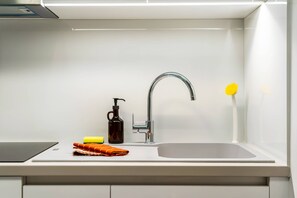 Eine moderne Küche mit Spüle aus Edelstahl, Wasserhahn, Seifenspender und einer gelben Blume.