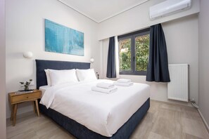 A modern hotel room with a large bed, a nightstand, a window with curtains, an air conditioning unit, and a blue abstract painting on the wall. - FiftySeven Athens - City Pulse, Balcony | 004 (Athina)