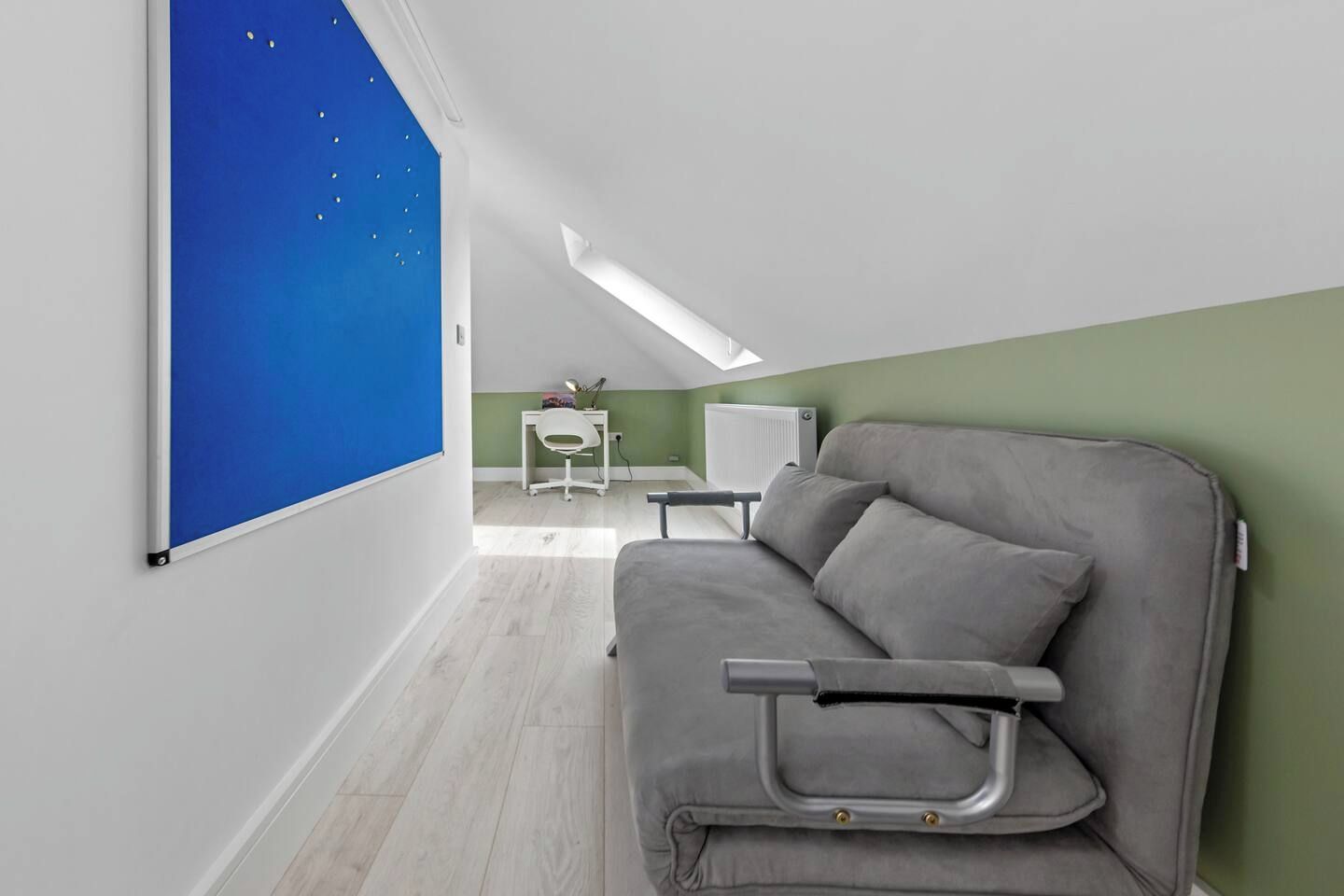 A room with a grey sofa, a small white desk, and a blue wall with stars.