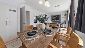A dining area with a wooden table set for four, surrounded by wicker chairs. - Welcome to our modern and spacious 6-bedroom, all en-suite home in **Northolt, West London**, perfect for **up to 12 guests**. Ideal for business travellers, contractors, families, relocation stays, and group trips. (Greater London)
