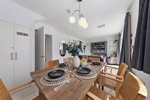 A dining area with a wooden table set for four, surrounded by wicker chairs. - Welcome to our modern and spacious 6-bedroom, all en-suite home in **Northolt, West London**, perfect for **up to 12 guests**. Ideal for business travellers, contractors, families, relocation stays, and group trips. (Greater London)