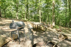 Et udendørs campingområde med grill, picnicbord og bålplads.