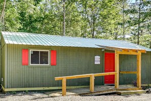 A small, single-story building with a green exterior and a red door, featuring a wooden ramp leading to the entrance. - Secluded Cabin with ATV Trails & Creek Access Near Ouachita National Forest, Arkansas (Langley)