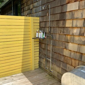 A wooden deck with a yellow fence, a metal showerhead, and a shelf with toiletries. - The Paradise Cabin w/ Sauna - 10 min to the Falls (Elka Park)