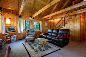 A cozy cabin interior with a leather sofa, armchair, and a television displaying a bear. - Secluded Island Park Cabin with Hot Tub Near Yellowstone & Henrys Lake, Idaho (Island Park)