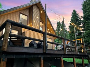 A wooden cabin with a deck, string lights, and outdoor seating. - Secluded Island Park Cabin with Hot Tub Near Yellowstone & Henrys Lake, Idaho (Island Park)