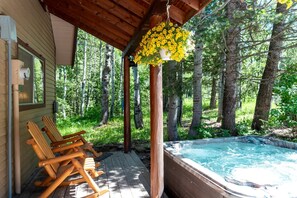 A wooden deck with Adirondack chairs, a hot tub, and a hanging flower basket. - Secluded Island Park Cabin with Hot Tub Near Yellowstone & Henrys Lake, Idaho (Island Park)