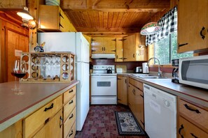 A compact kitchen with wooden cabinets, a white refrigerator, a stove, a microwave, and a sink. - Secluded Island Park Cabin with Hot Tub Near Yellowstone & Henrys Lake, Idaho (Island Park)