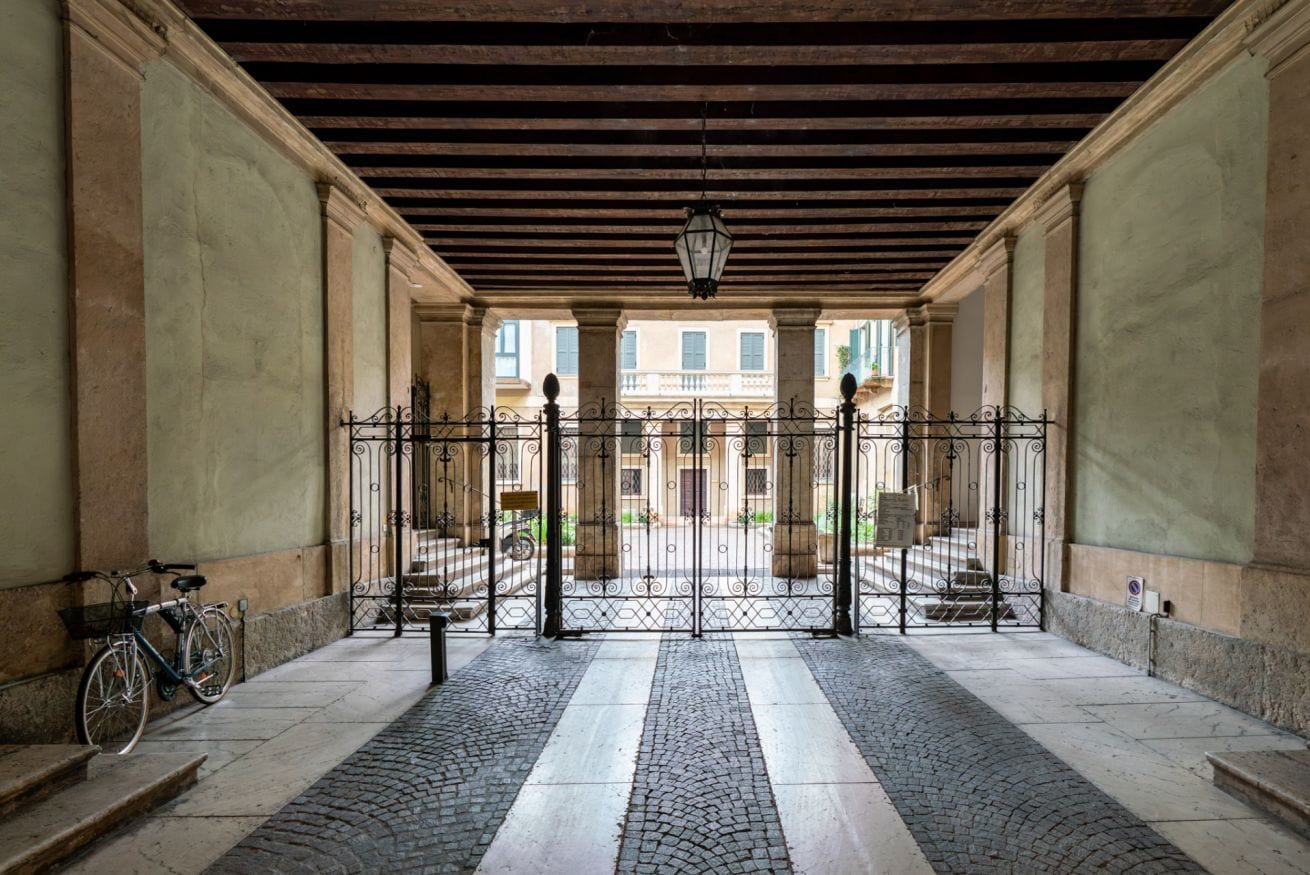 A covered courtyard with a wrought iron gate, a bicycle, and a cobblestone path.