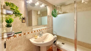 Een badkamer met een wastafel, spiegel, douche en decoratieve planten.