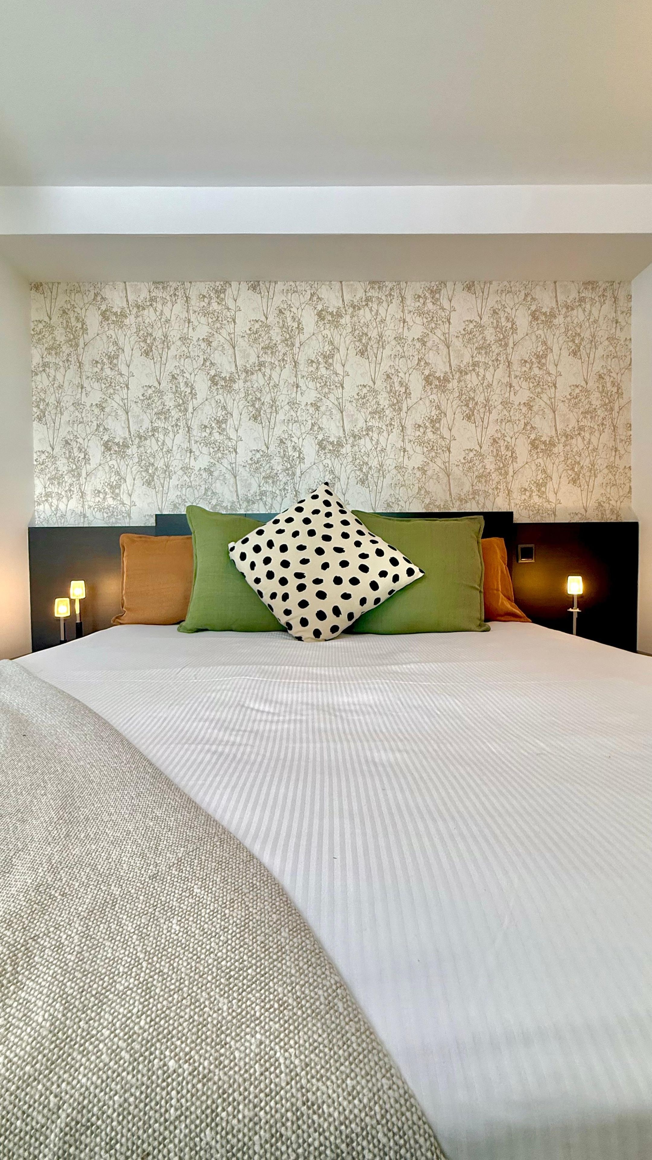 Hotellihuone, jossa on suuri sänky, kaksi yöpöytävalaisinta ja kukkakuviotapetti.