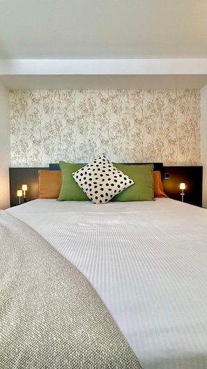 Een hotelkamer met een groot bed, twee bedlampen en behang met bloemenmotieven.