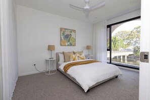 A bedroom with a bed, two bedside tables, a ceiling fan, a window with a view, and a wall-mounted artwork. - Waterfront 4BD Terrace with Pool, Gold Coast (Bundall)