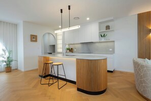 A modern kitchen with a central island, two bar stools, pendant lighting, and a built-in oven. - Waterfront 4BD Terrace with Pool, Gold Coast (Bundall)