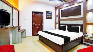 Une chambre d’hôtel avec un lit, un bureau avec une télévision, un ventilateur de plafond et une porte.