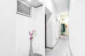 A hallway with a framed picture on the wall, a vase with flowers, and a fire extinguisher mounted on the wall.
