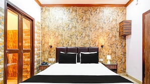 Une chambre d’hôtel avec un grand lit, une tête de lit en bois, un mur décoré d’un motif marbré, une armoire en bois et une table de chevet avec une lampe.