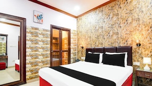 Une chambre d’hôtel avec un lit, un miroir, une chaise rouge, un mur orné d’un motif géométrique et une porte donnant sur une salle de bain.