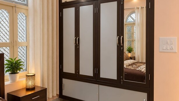 Ein Schlafzimmer mit großem Kleiderschrank, Nachttisch mit Lampe und einem fenster mit Vorhängen.
