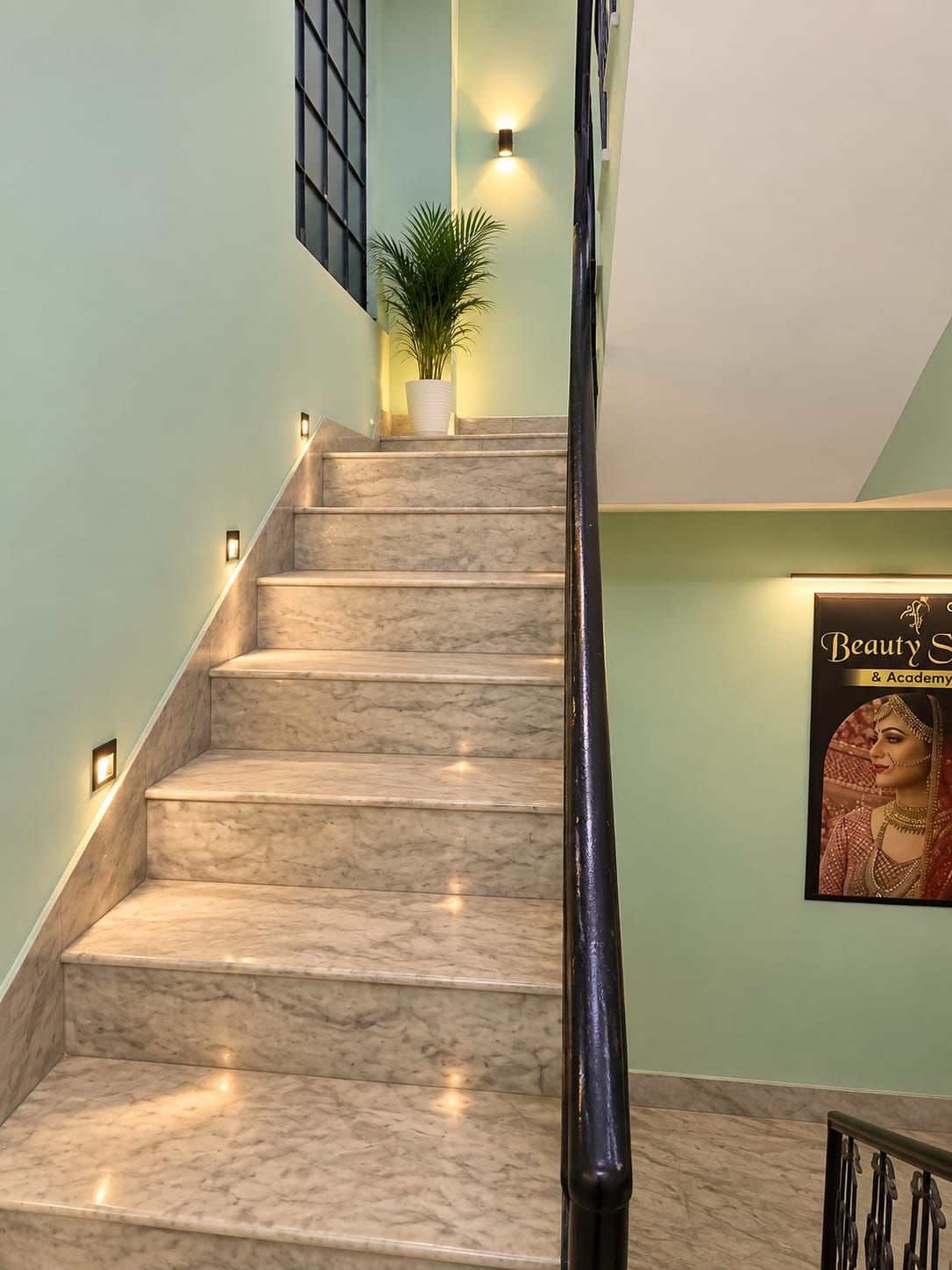 A marble staircase with wall-mounted lights, a potted plant, and a poster on the wall.