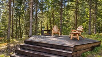 A wooden deck with two Adirondack chairs and a small table, surrounded by a forest.