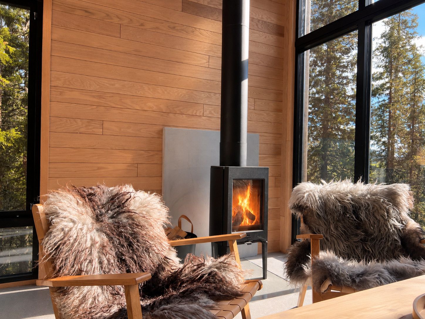 Un intérieur moderne avec un poêle à bois, des murs en bois et de grandes fenêtres donnant sur une forêt.