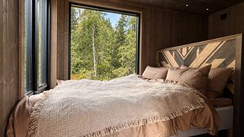 A bedroom with a large window, a bed with a patterned blanket, and a wooden headboard.