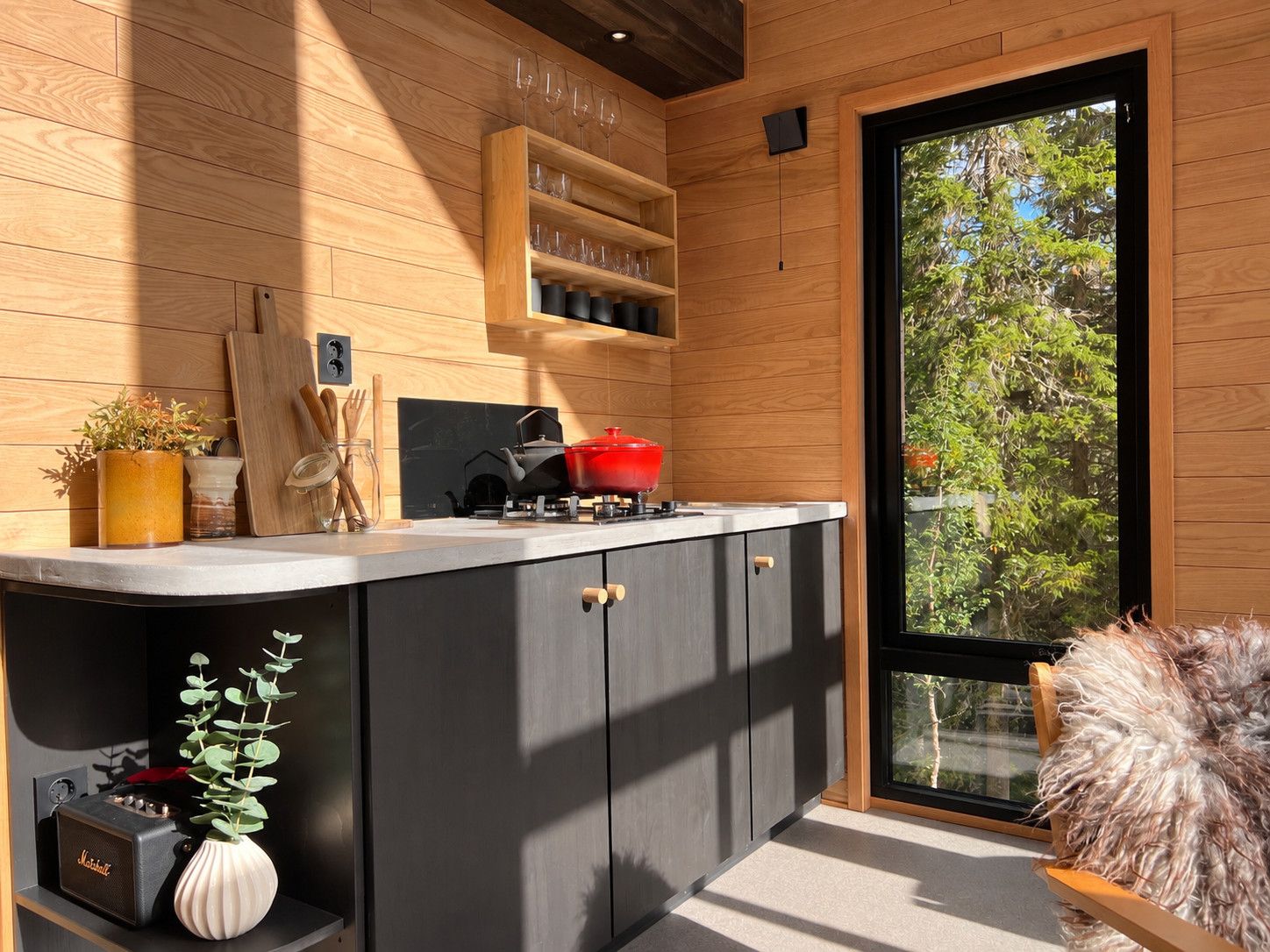 A modern kitchen with wooden cabinetry, a black countertop, and a large window offering a view of trees.