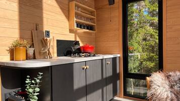 A modern kitchen with wooden cabinetry, a black countertop, and a large window offering a view of trees.