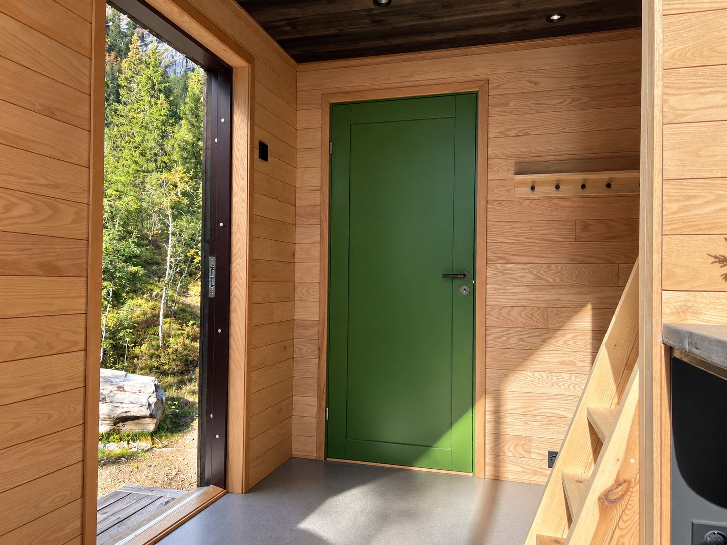 Un intérieur en bois avec une porte verte, une petite fenêtre et un banc en bois.